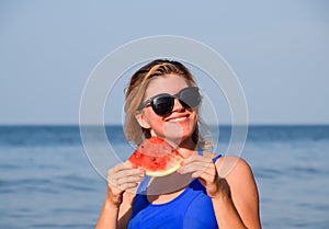 A blonde in sunglasses eats a watermelon by the sea. A juicy watermelon in the hands of a woman