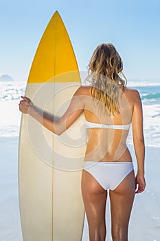 Blonde surfer in white bikini holding her board on the beach