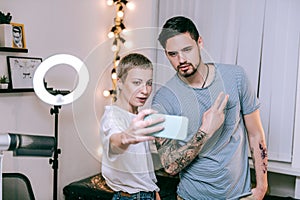 Blonde tattoo artist and her regular customer making selfie after long session