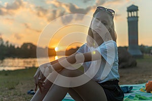 Blonde teen girl sitting by the lake in the park and resting