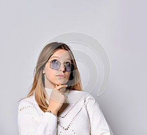 Blonde teenager in sunglasses, smart watch, bracelet and sweater. She is looking thoughtful, posing isolated on white. Close up