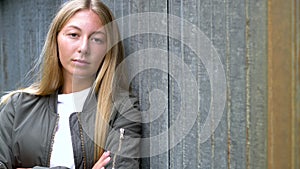 Blonde teenager young woman looking sad or thoughtful wearing a green jacket in an urban city environment