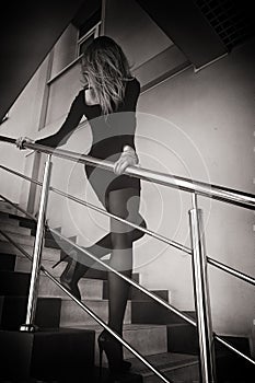 blonde total black in a short dress, stockings and black stiletto shoes strolls down the stairs
