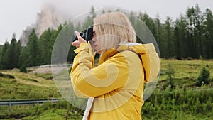 Blonde tourist makes photos of meadows of Alpine mountain