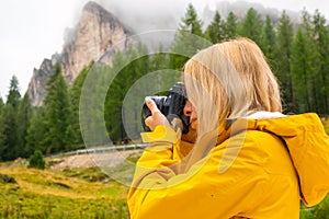 Blonde tourist makes photos of meadows of Alpine mountain