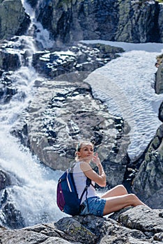 A blonde tourist is sitting on a rock above the Siklawa waterfall in the Polish Tatra Mountains.