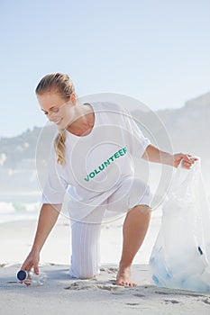 Blonde volunteer picking up trash on the beach