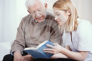 Blonde volunteer reading book to senior man in nursing home