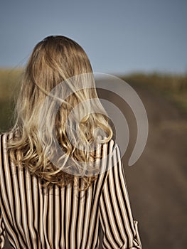 The blonde is walking along a country road in a striped dress from the back