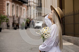 blonde in a white sundress dress with a bouquet of daisies. Walk around the city