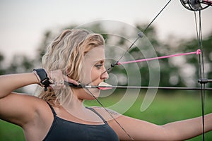 Blonde woman aiming a hunting bow in a wooded area