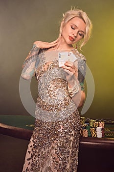 Blonde woman with a beautiful hairstyle and perfect make-up is posing with two playing cards in her hands. Casino, poker
