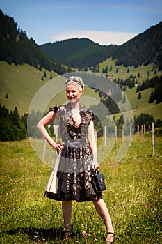 Blonde woman in black dirndl with bag and stylish hairstyle