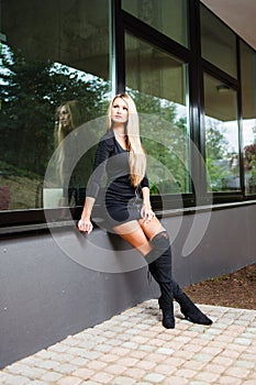 Blonde woman in black short dress sitting on windowsill