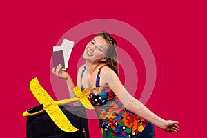 A blonde woman in bright clothes with documents, a suitcase and a bright yellow toy plane, happy to travel and posing on