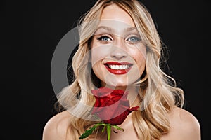 Blonde woman with bright makeup red lips posing isolated over black wall background holding rose flower