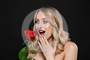 Blonde woman with bright makeup red lips posing isolated over black wall background holding rose flower
