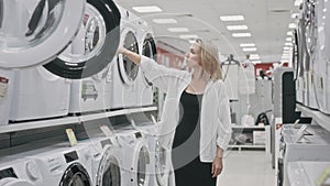 A blonde woman chooses a washing machine in an electronics hypermarket among a large range of products