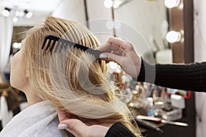 A blonde woman is combing her hair in a professional beauty salon. Beauty and care. Close-up. Back view