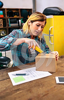 Blonde woman with cutter unpacking order received by courier with merchandise to sell on line