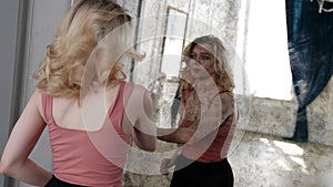 blonde woman is dancing and looking to vintage wall mirror, viewing reflection of young man