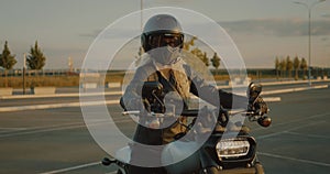 Blonde woman dressed in black helmet mask, leather jacket sitting on motorbike