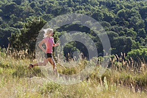 Blonde woman on early morning run with distant tree background.
