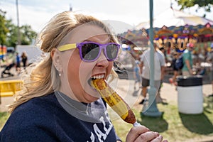 Blonde woman eats a pronto pup corn dog covered in mustard at an outdoor fair photo