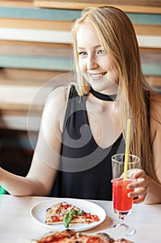 Blonde woman in elegant black dress drinking pink beverage at restaurant