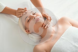 blonde woman enjoying facial massage lying on spa bed indoor