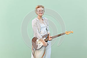 Blonde woman with eyeglasses, holding guitar and looking at camera with smile.