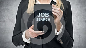 Blonde woman in formal suit presents a tablet with the words 'Job Search' on the screen. A concept of recruitment process. Interns