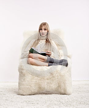 Blonde woman on furry arm-chair with book in hands