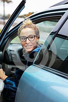 Blonde woman with glasses look back over her shoulder she get out of parked car in which she drove