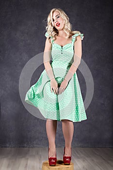 Blonde woman with hair in the wind. girl with flying hair posing in green dress and red shoes