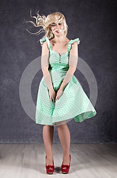Blonde woman with hair in the wind. girl with flying hair posing in green dress and red shoes