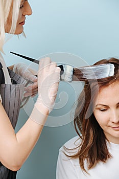 Blonde woman hairdresser applying developer on client`s hair over blue
