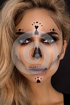 Blonde woman in Halloween makeup and leather outfit on a black background in the studio. Skeleton, monster and witch.