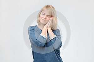 Blonde woman with happy serene face standing asleep pretending sleeping with head on hands