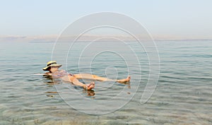Blonde woman with hat floating in the turquoise waters of the Dead Sea