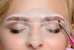 Blonde woman having permanent make-up tattoo on her eyebrows. Closeup beautician doing tattooing eyebrow. Green eyes close up.