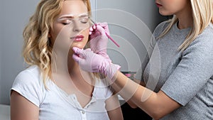 Blonde woman having permanent make-up tattoo on her eyebrows. Closeup beautician doing tattooing eyebrow.Professional makeup and