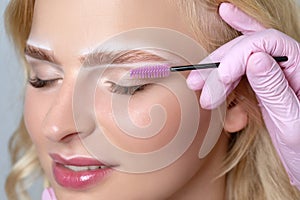 Blonde woman having permanent make-up tattoo on her eyebrows. Closeup beautician doing tattooing eyebrow.Professional makeup and