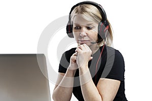 A blonde woman with headphones and a microphone sits at a table with a laptop. Remote work, distance learning and support service