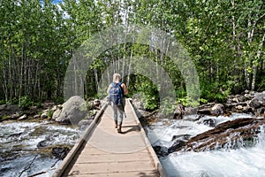 Blonde woman hiker crosses the bridge acress the creek along the Bradley Lake hike in Grand Teton National Park