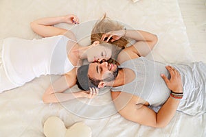 Blonde woman and hispanic man lying in bad in morning, monophonic background.
