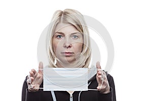 A blonde woman is holding a medical mask in front of her. Precautions during seasonal allergies. Self-isolation mode in the