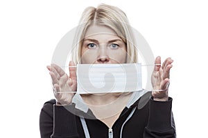 A blonde woman is holding a medical mask in front of her. Precautions during seasonal allergies. Self-isolation mode in the