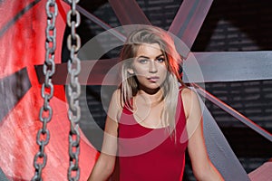 Blonde woman in industrial theme location with red neon light in background