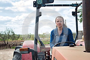 Blonde woman in jeans riding on a red tractor ready to work in the field